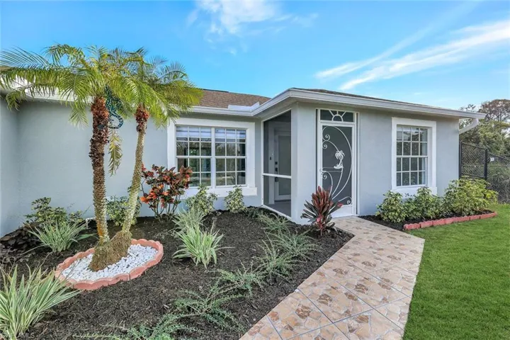 Doorway to property with roof with shingles, a lawn, and stucco siding