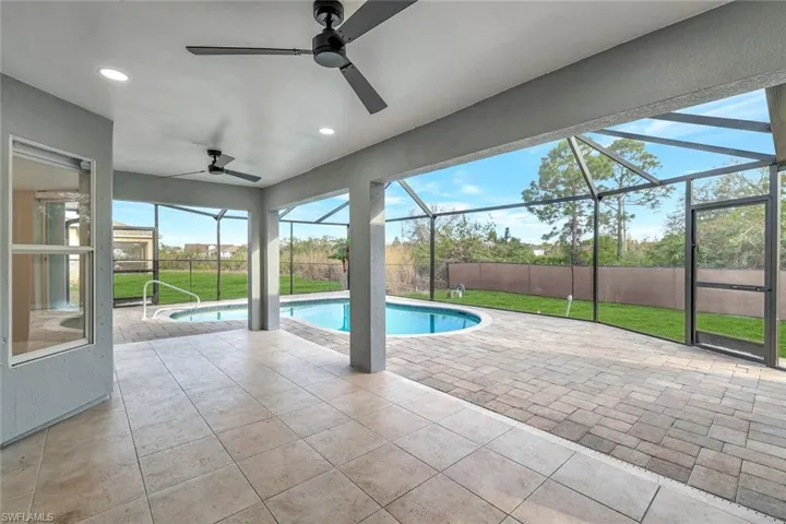 View of swimming pool with glass enclosure, a patio area, a ceiling fan, and a lawn