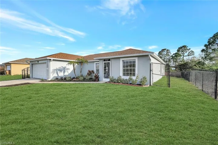 View of front of home featuring stucco siding, a front yard, fence, a garage, and driveway