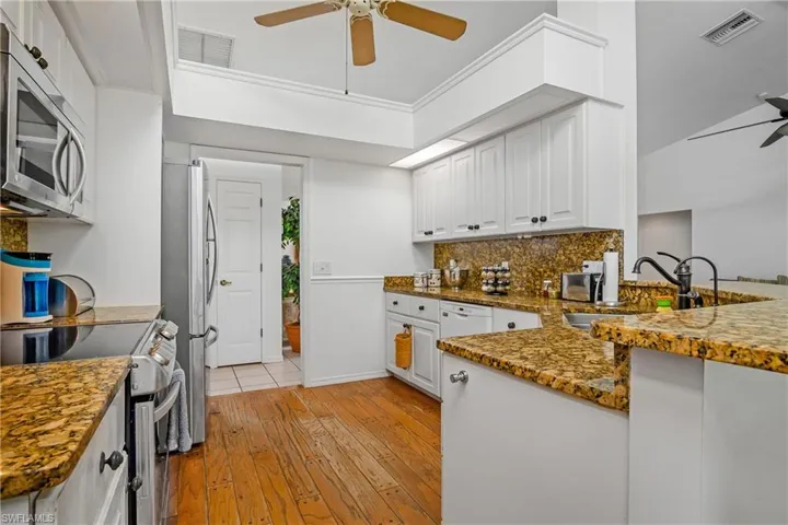 Kitchen with white cabinetry, ceiling fan, light wood-type flooring, appliances with stainless steel finishes, and kitchen peninsula