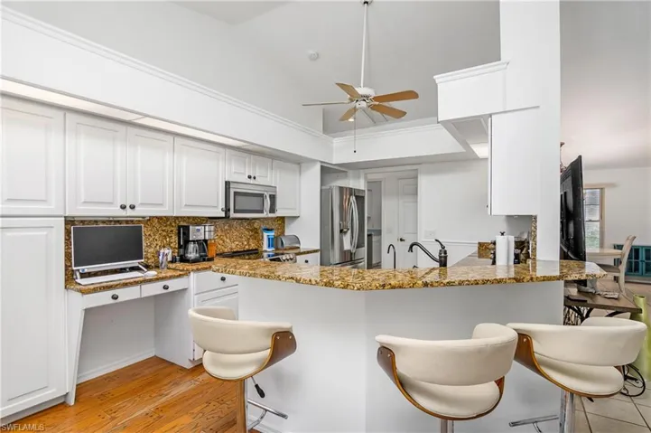 Kitchen with ceiling fan, stainless steel appliances, light stone countertops, light hardwood / wood-style flooring, and kitchen peninsula