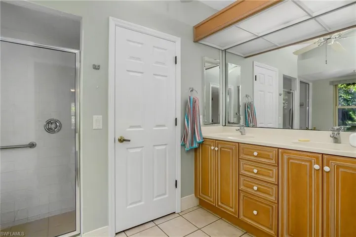 Bathroom featuring a shower with door, tile patterned floors, ceiling fan, and dual bowl vanity