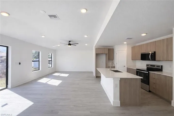 Kitchen with stainless steel appliances, modern cabinets, light wood-style floors, a center island with sink, and open floor plan