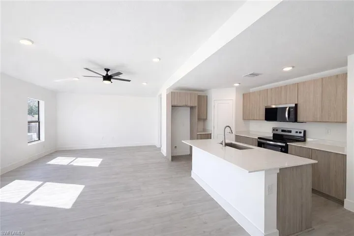 Kitchen featuring modern cabinets, stainless steel appliances, an island with sink, light wood-style floors, and light stone counters