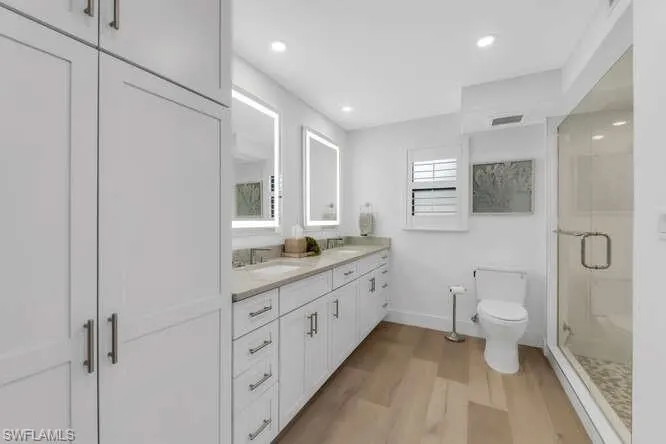 Bathroom featuring toilet, wood finished floors, a shower stall, baseboards, and double vanity