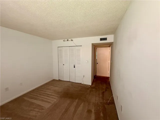 Unfurnished bedroom with a textured ceiling, dark carpet, and a closet