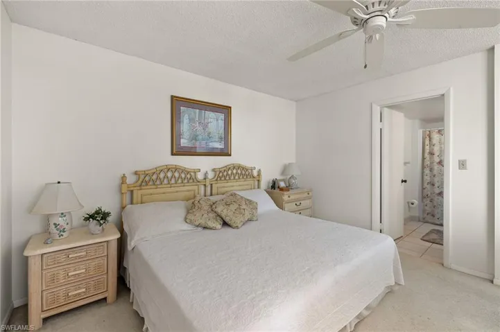 Bedroom featuring ensuite bathroom, a textured ceiling, light tile patterned floors, light colored carpet, and ceiling fan
