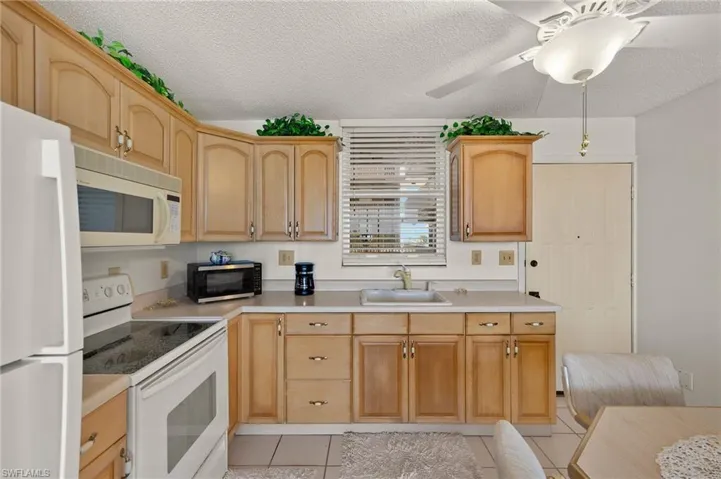 Kitchen featuring white appliances, light tile patterned floors, a sink, light countertops, and a textured ceiling