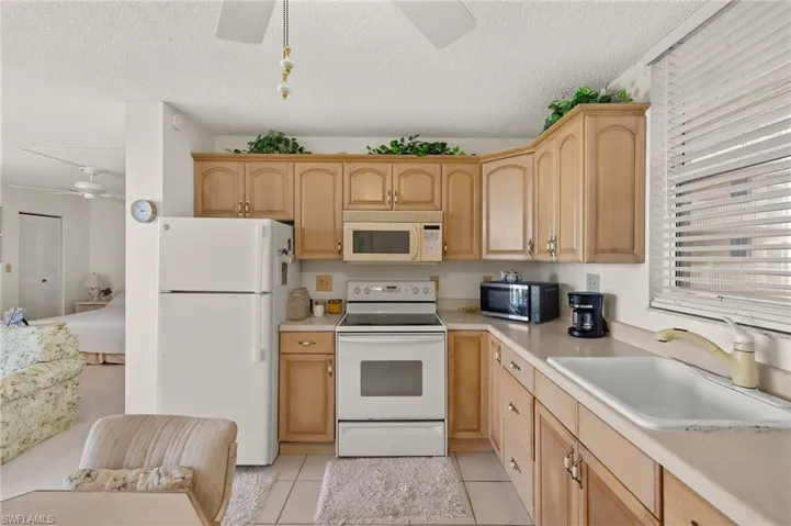 Kitchen with a ceiling fan, a sink, white appliances, light countertops, and light tile patterned floors