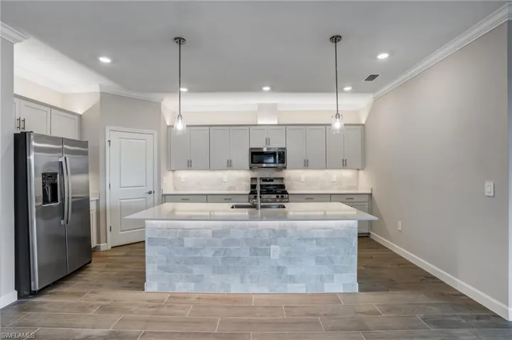 Kitchen with appliances with stainless steel finishes, a sink, crown molding, wood finish floors, and light countertops