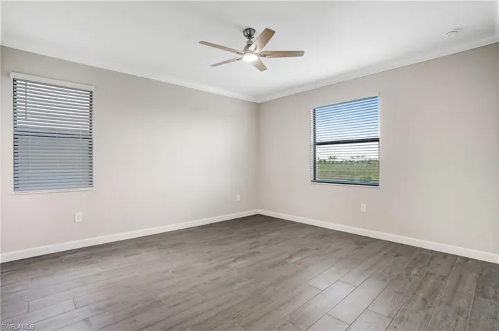 Unfurnished room featuring ceiling fan, crown molding, dark wood-style flooring, and baseboards