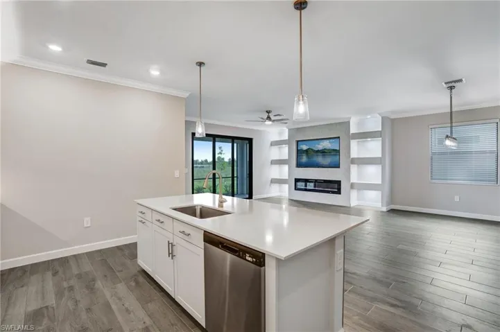 Kitchen with stainless steel dishwasher, a sink, ornamental molding, pendant lighting, and an island with sink