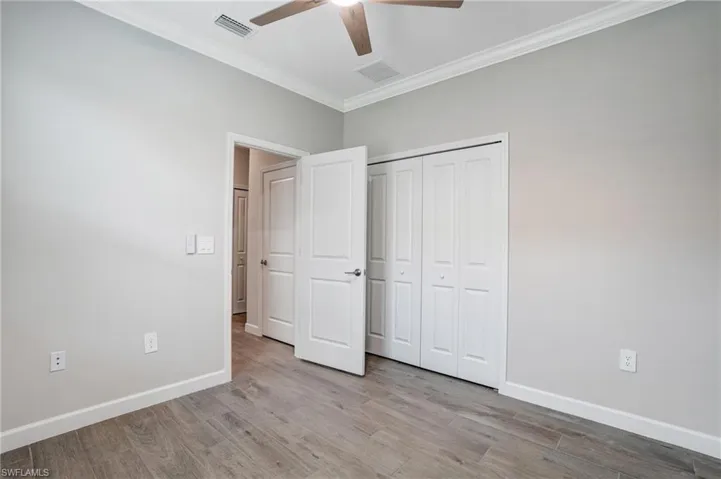 Unfurnished bedroom with crown molding, wood finished floors, baseboards, a closet, and ceiling fan