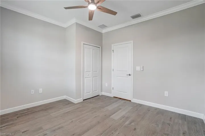 Unfurnished bedroom featuring light wood-style floors, ornamental molding, baseboards, ceiling fan, and a closet