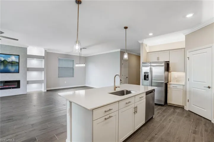 Kitchen featuring a sink, appliances with stainless steel finishes, ornamental molding, open floor plan, and dark wood finished floors