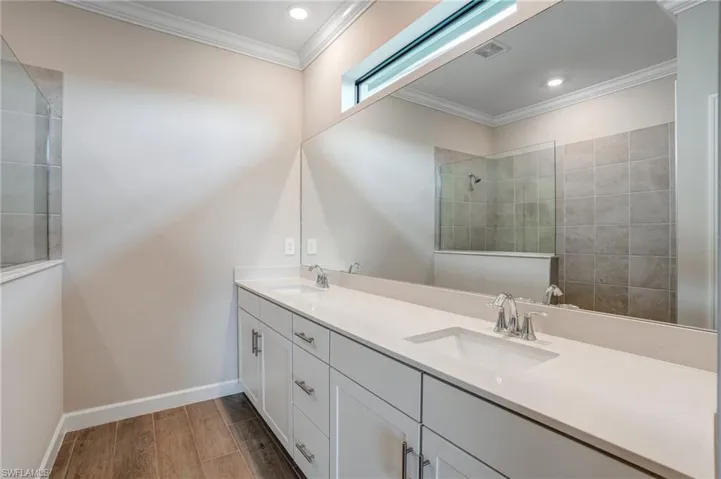 Full bath with double vanity, wood finished floors, ornamental molding, baseboards, and walk in shower
