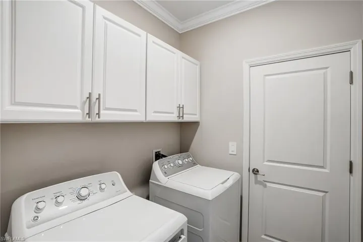 Laundry area featuring independent washer and dryer, cabinet space, and crown molding