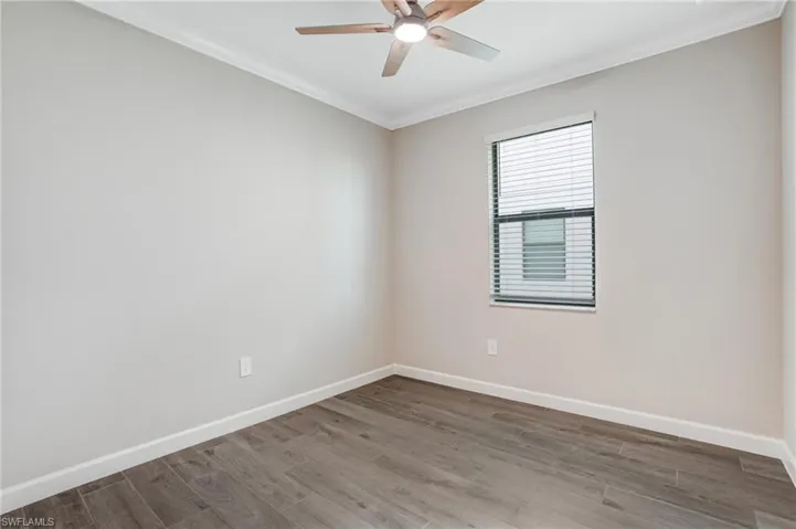 Spare room with ornamental molding, wood finished floors, a ceiling fan, and baseboards