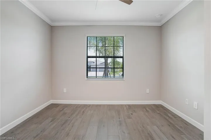 Spare room with wood finished floors, crown molding, baseboards, a ceiling fan, and a smoke detector