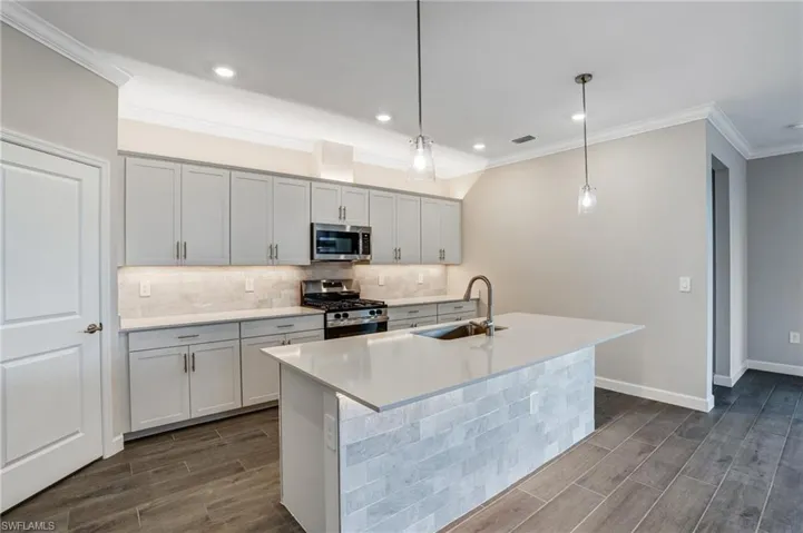 Kitchen with appliances with stainless steel finishes, a sink, wood tiled floors, tasteful backsplash, and ornamental molding