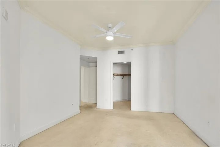 Unfurnished bedroom featuring a ceiling fan, crown molding, a walk in closet, and light colored carpet