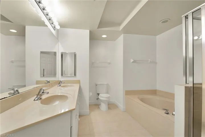 Bathroom featuring a garden tub, a shower stall, double vanity, light tile patterned floors, and recessed lighting