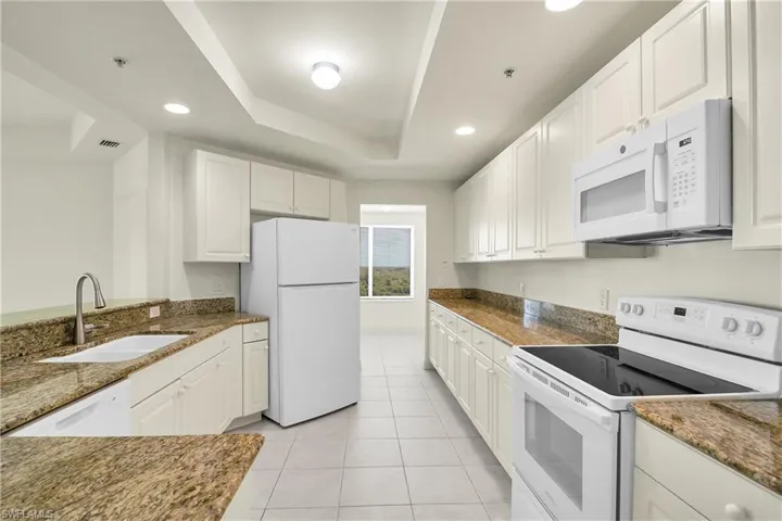 Kitchen featuring white appliances, a tray ceiling, recessed lighting, white cabinetry, and dark stone counters