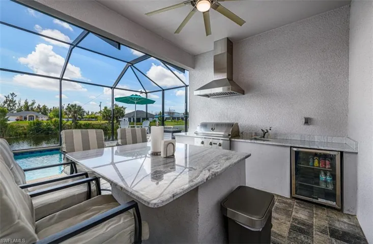 LARGE SPACTIOUS OUTDOOR KITCHEN WITH STAINLESS STEEL GRILLAND OVERHEAD RANGE HOOD AND WINE COOLER