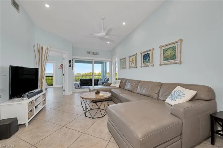 Living room with ceiling fan, light tile patterned flooring, and vaulted ceiling