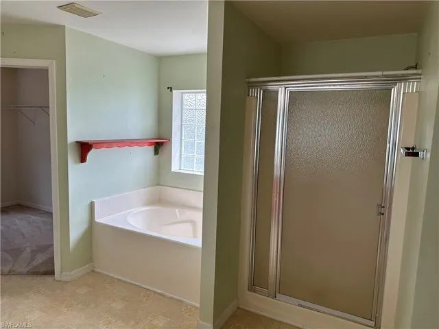 Bathroom featuring a walk in closet, baseboards, a stall shower, a garden tub, and visible vents