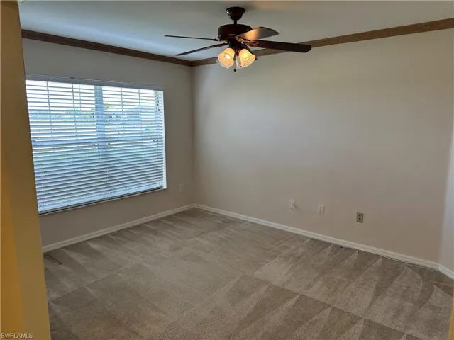 Unfurnished room featuring light colored carpet, ornamental molding, ceiling fan, and baseboards