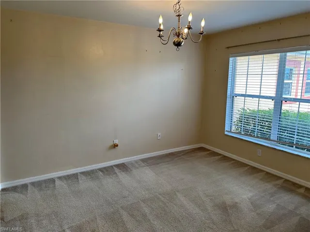 Carpeted spare room featuring baseboards and a chandelier