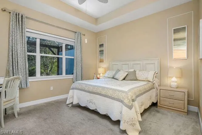 Owner's suite featuring light colored carpet, ceiling fan, and a tray ceiling