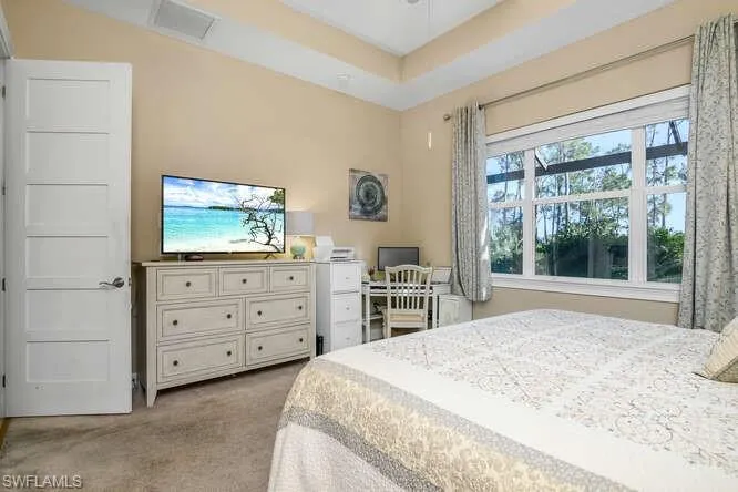 Owner's Bedroom featuring light colored carpet, large section of windows looking out at the pool, pond and treed lot.