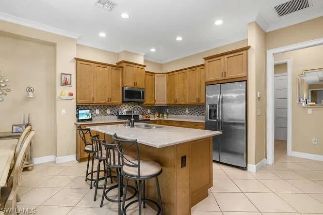Kitchen featuring stainless steel appliances, wood finish cabinets, a center island with sink, a kitchen bar, and ornamental molding