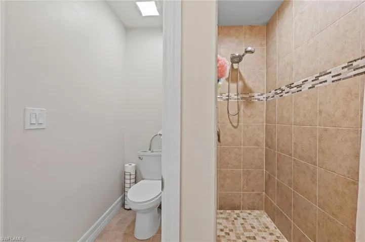 Bathroom featuring baseboards, toilet, tile patterned flooring, and a stall shower