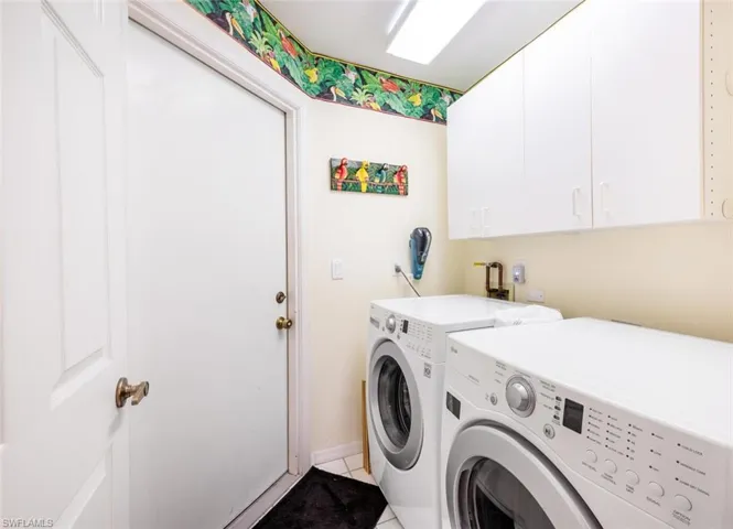 Clothes washing area featuring light tile patterned floors, cabinets, and washer and clothes dryer
