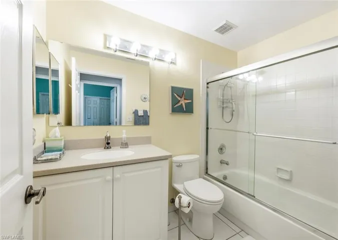 Full bathroom with toilet, tile patterned flooring, enclosed tub / shower combo, and vanity