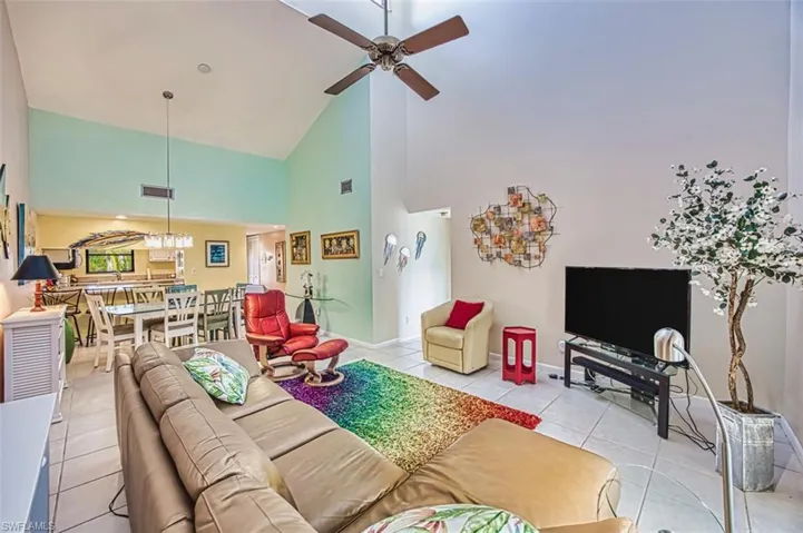 Living room with high vaulted ceiling, light tile patterned flooring, and a ceiling fan