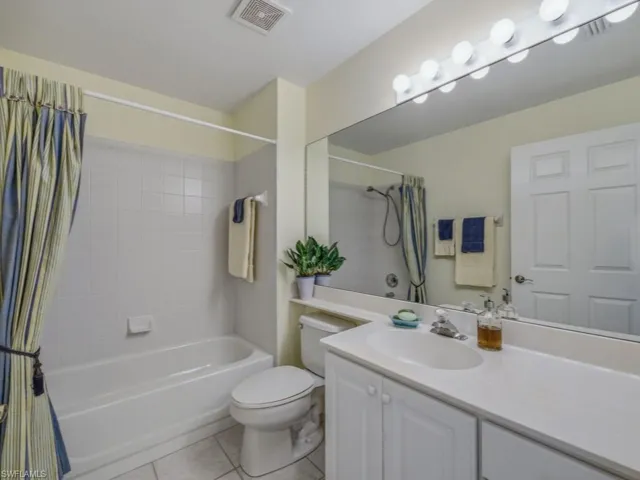 Full bath featuring vanity, shower / tub combo with curtain, and light tile patterned floors