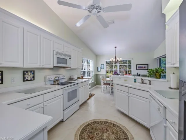 Kitchen featuring white appliances, lofted ceiling, light countertops, a peninsula, and a chandelier