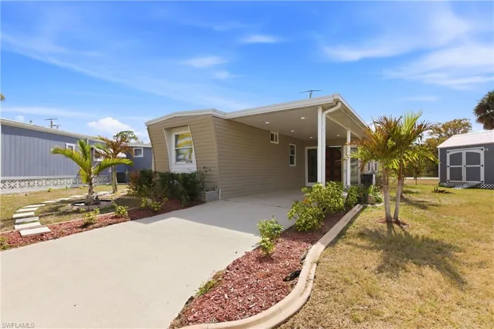 View of front of house featuring an attached carport, driveway, a front yard, and an outdoor structure