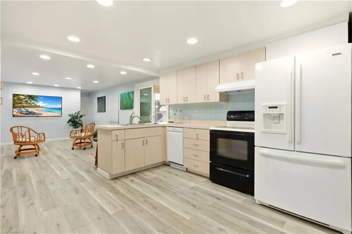 Kitchen with a peninsula, white appliances, light countertops, light wood finish cabinetry, and tasteful backsplash