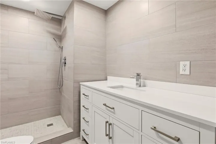 Bathroom with vanity, tiled shower, and tile walls