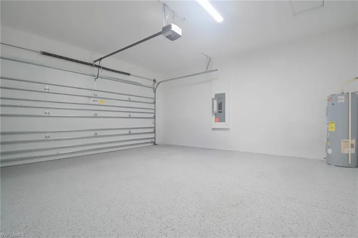 Garage featuring electric panel, a garage door opener, and water heater