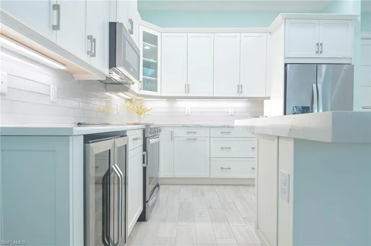 Kitchen with white cabinets, light hardwood / wood-style flooring, appliances with stainless steel finishes, wine cooler, and tasteful backsplash