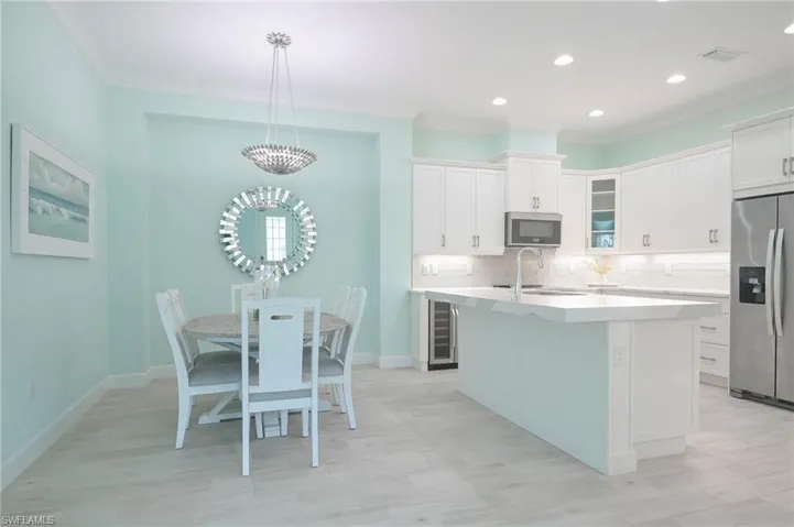 Kitchen featuring pendant lighting, appliances with stainless steel finishes, an island with sink, light wood-type flooring, and white cabinets