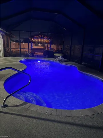 Pool at night with an outdoor pool, a sunroom, and glass enclosure
