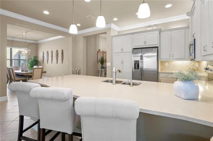 Kitchen featuring pendant lighting, stainless steel appliances, a kitchen breakfast bar, light stone countertops, and crown molding
