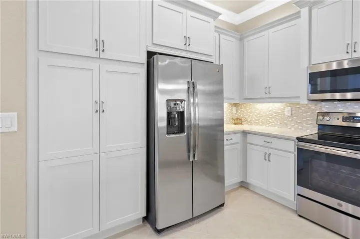 Kitchen featuring appliances with stainless steel finishes, white cabinets, light stone counters, light tile patterned flooring, and decorative backsplash
